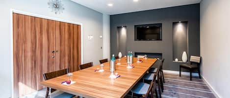 A conference room with a long wooden table, blue chairs, and a modern clock on the wall.