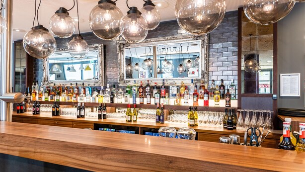 A bar area with a variety of liquor bottles, glasses, and a mirror above the counter.