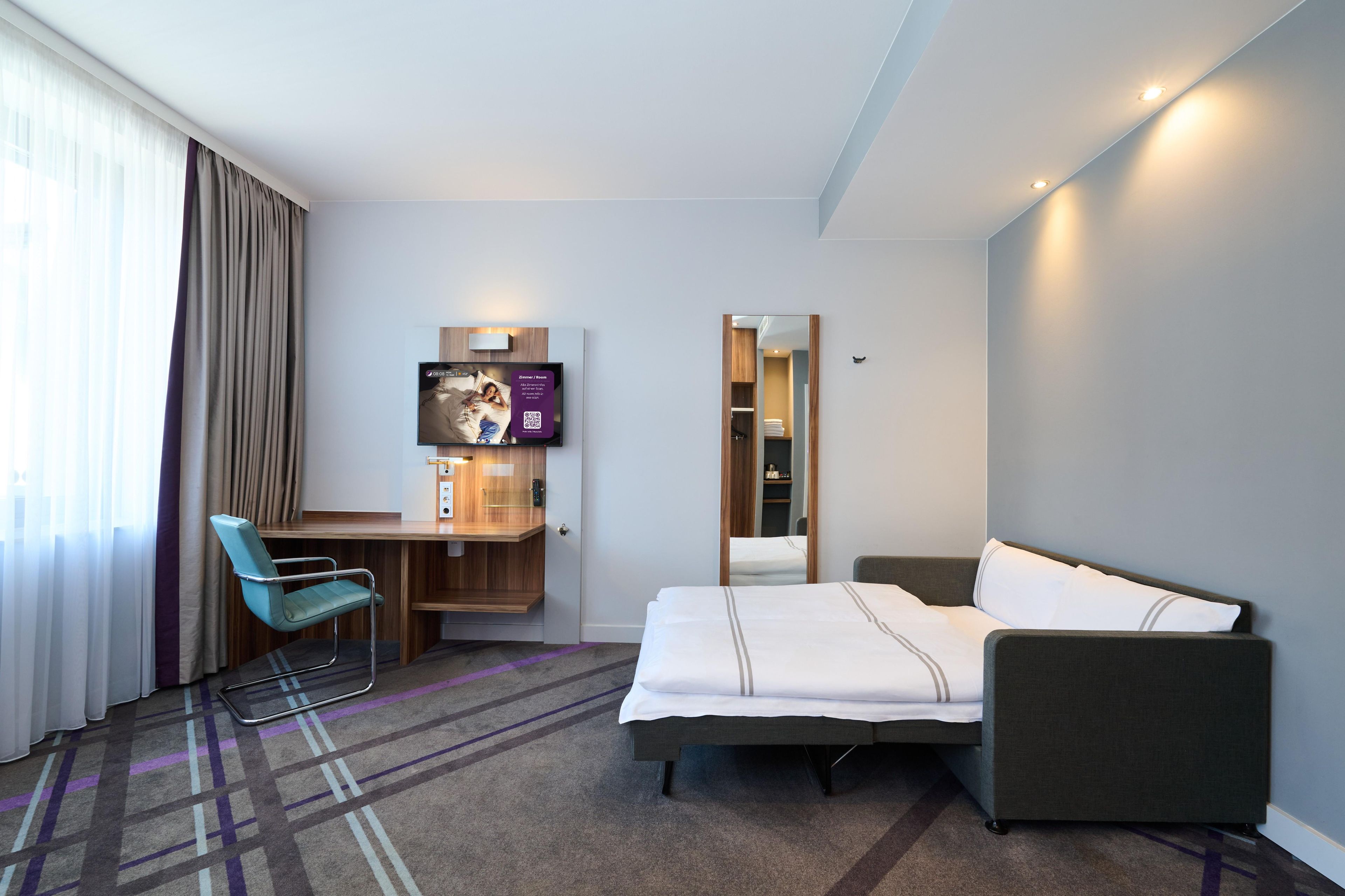 A hotel room with a bed, a desk, a chair, a TV, and a mirror.
