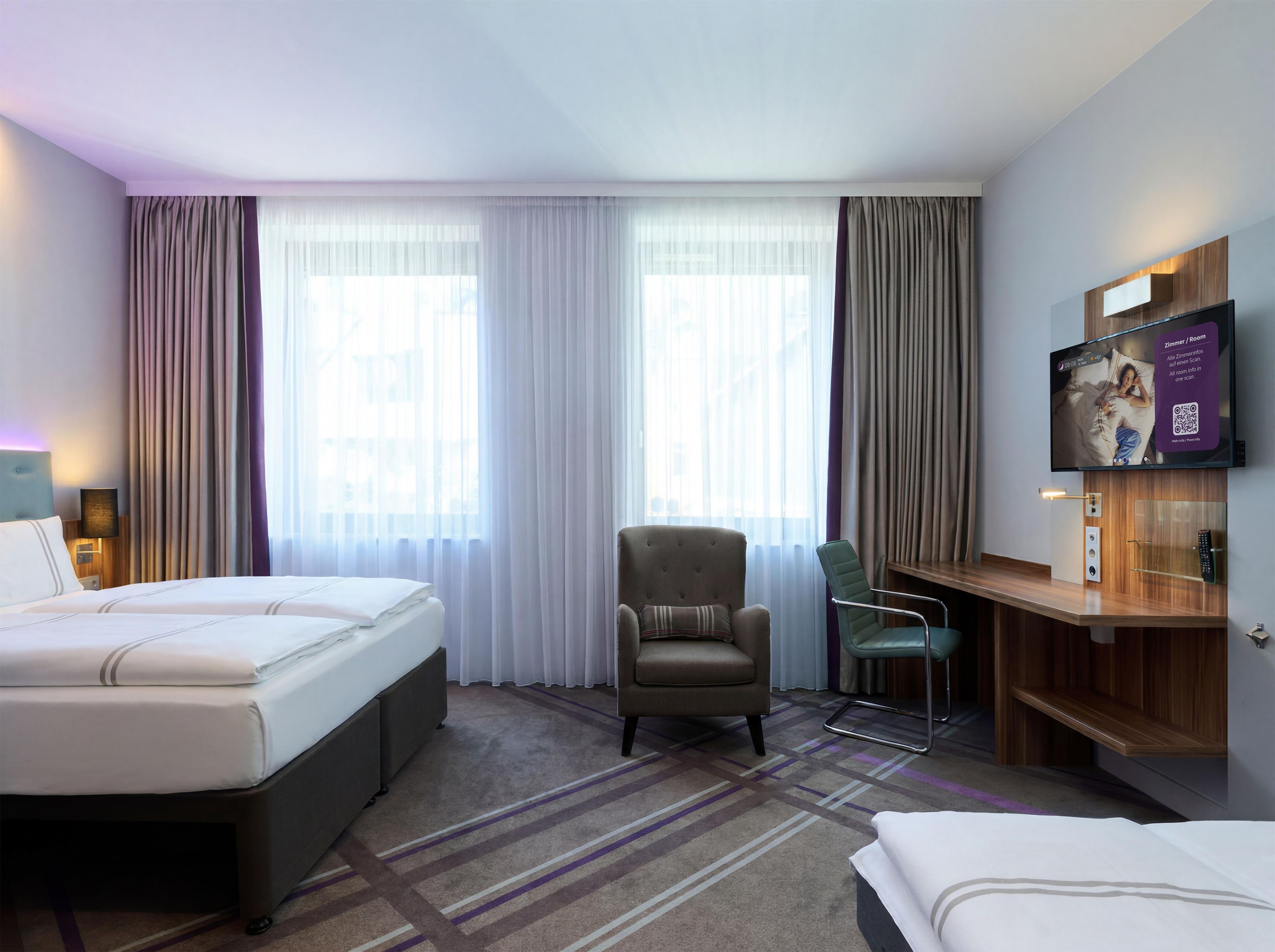 A hotel room with a bed, a chair, a TV, and a desk.
