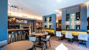 Un restaurante moderno con zona de bar, diferentes distribuciones de mesas y una exhibición de alimentos para el desayuno.