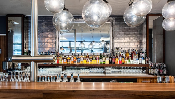 Una zona de bar con mostrador de madera, lámparas esféricas colgantes y pared de ladrillo.