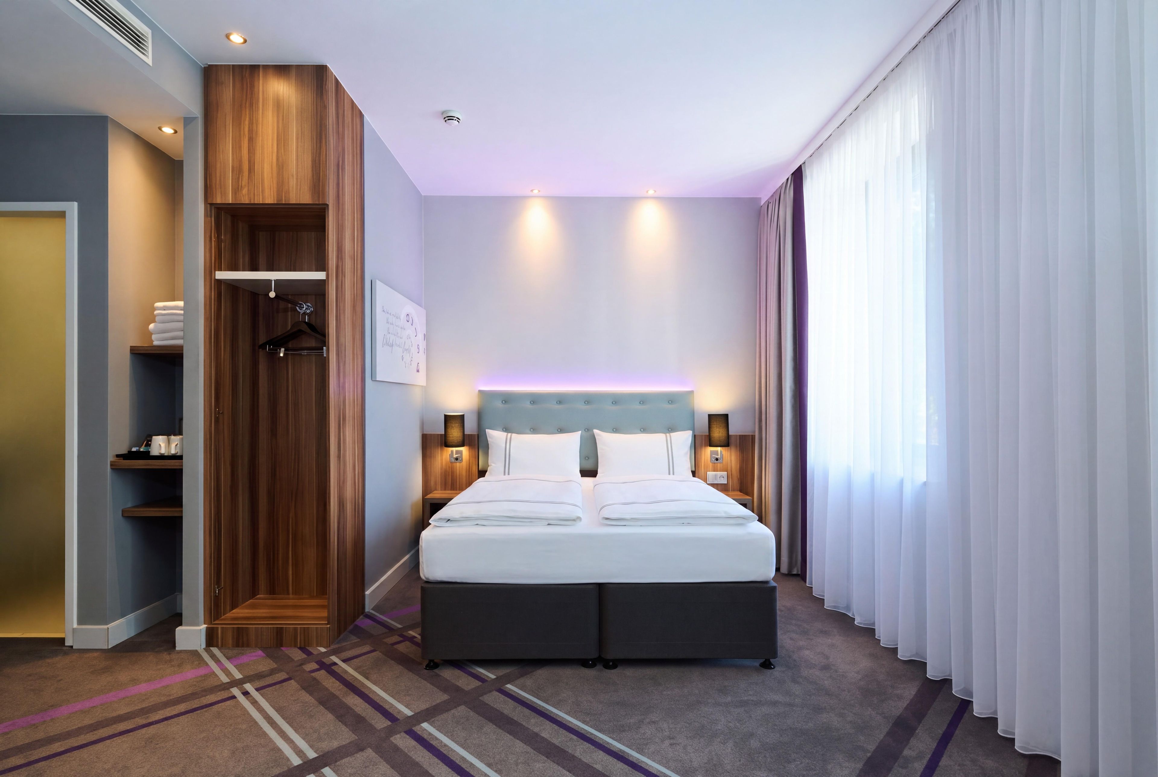 Une chambre d’hôtel avec un lit, des tables de chevet, une armoire et une fenêtre avec des rideaux.