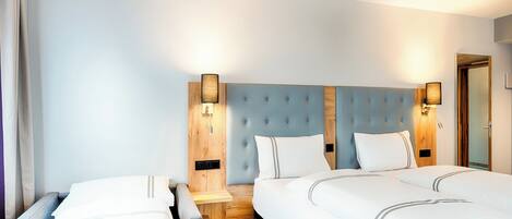A hotel room with two beds, a wooden headboard, and two wall-mounted lamps.