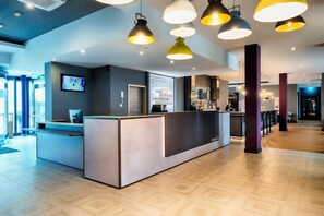 A reception area with a counter, a TV screen, and a digital display. - Premier Inn Lindau (Lindau)