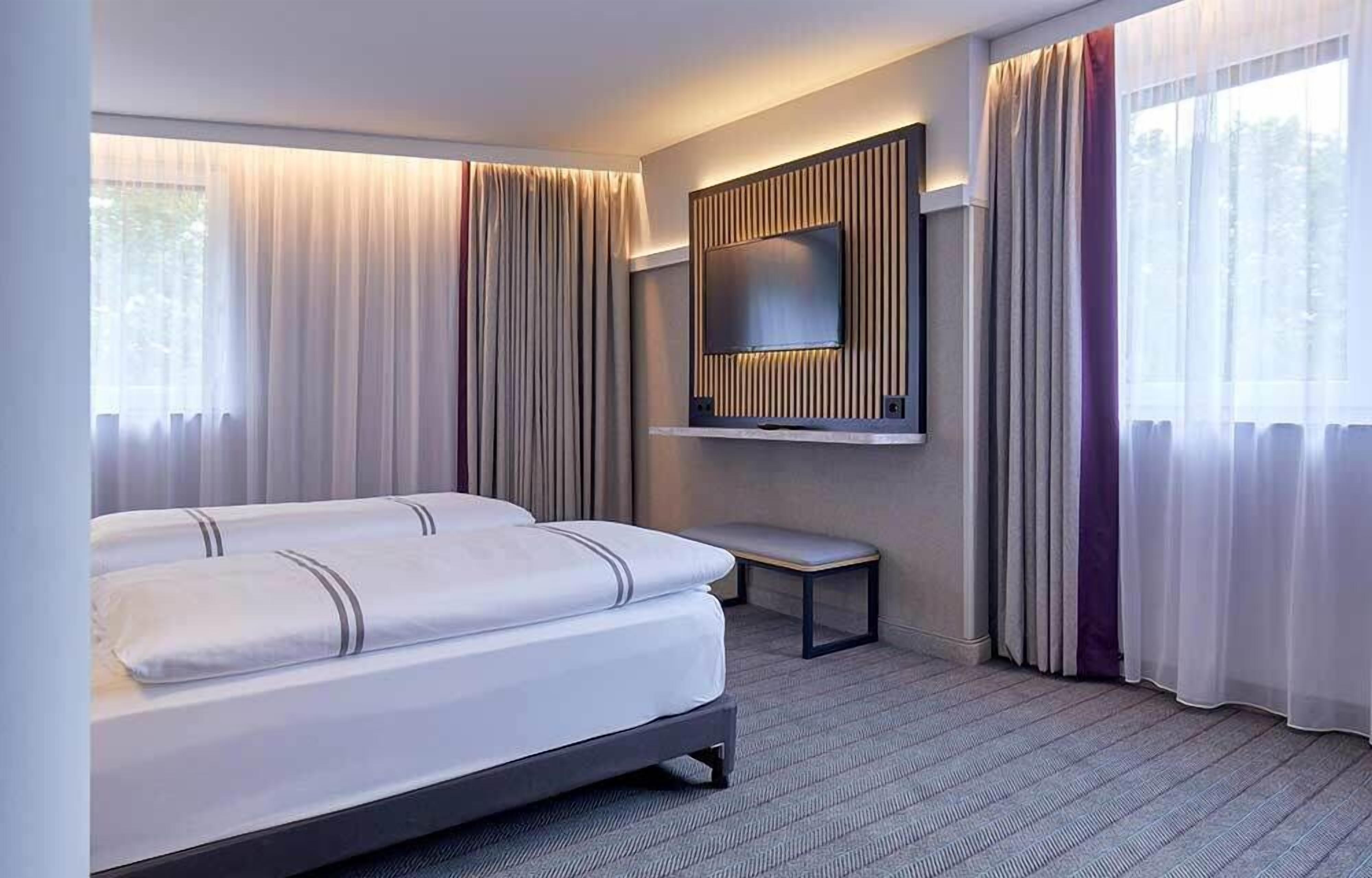 A modern hotel room with a large bed, a small desk, and a TV mounted on the wall.