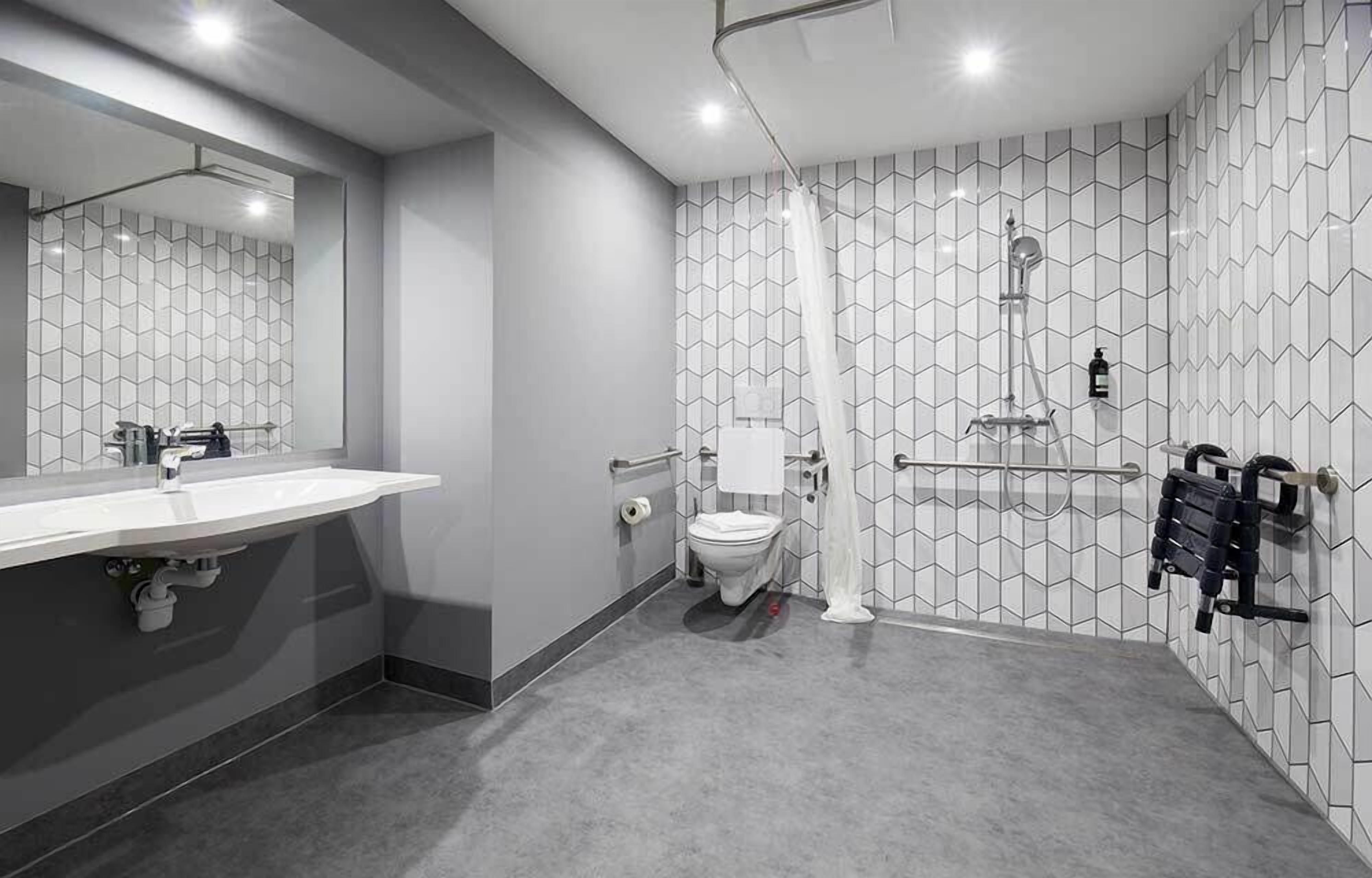 Ein modernes Badezimmer mit großem Spiegel, Waschbecken in Weiß, Toilette und Duschbereich.