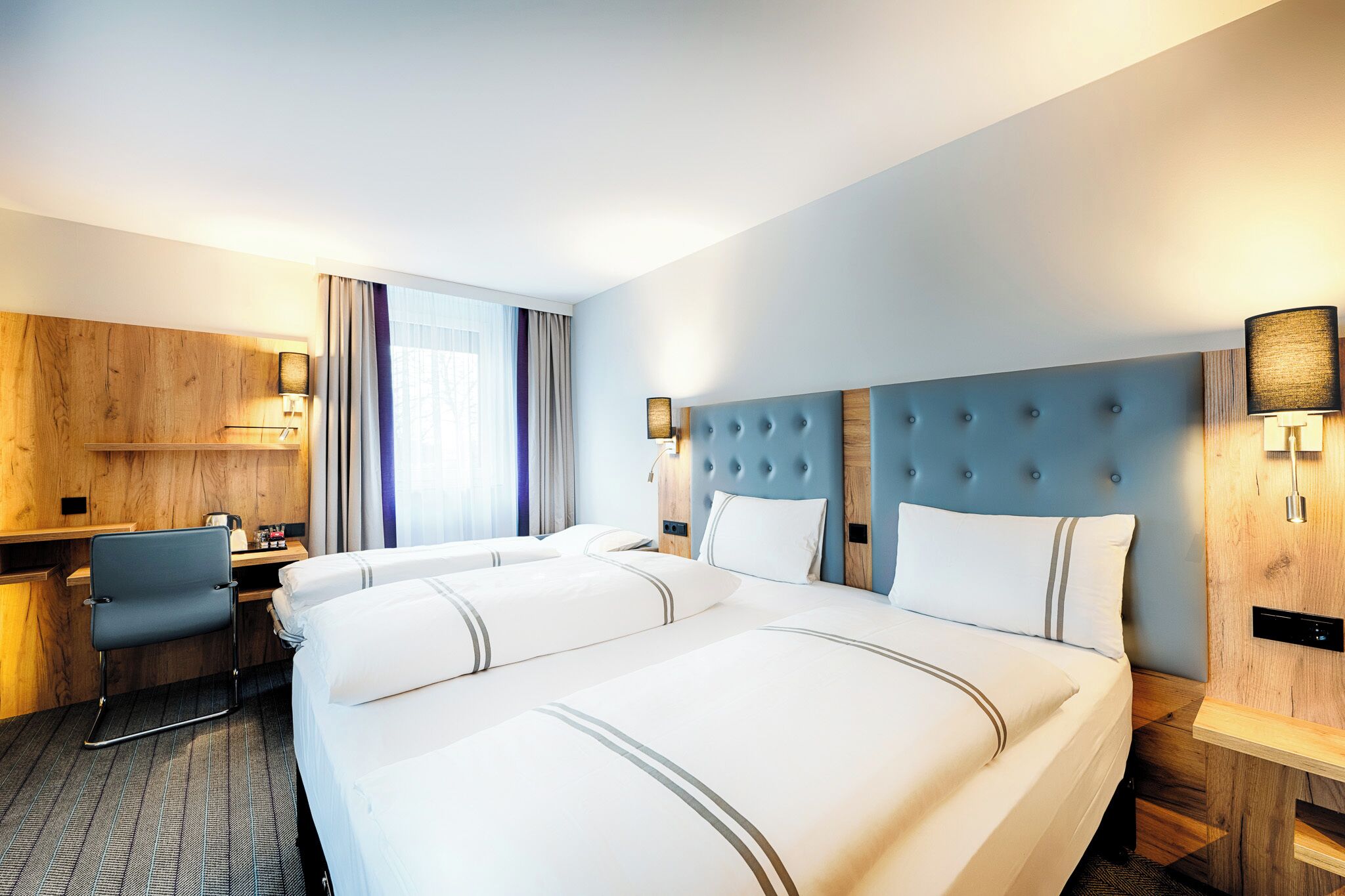 A hotel room with a large bed, a desk, and a chair.
