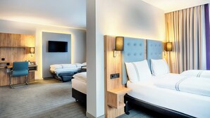 A hotel room with a large bed, a desk with a chair, a television, and a wall-mounted lamp. - Premier Inn Lindau (Lindau)