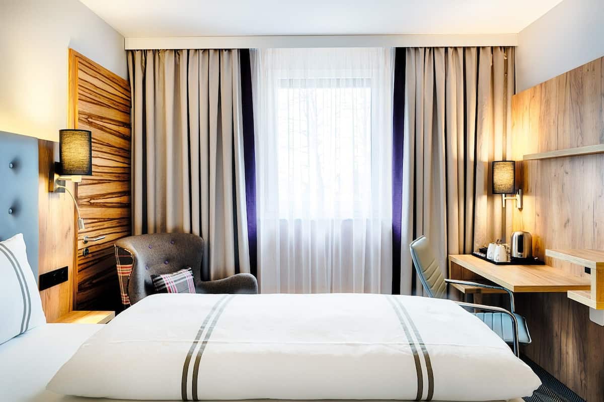 A hotel room with a large bed, a desk, a chair, a wardrobe, and a window with curtains.