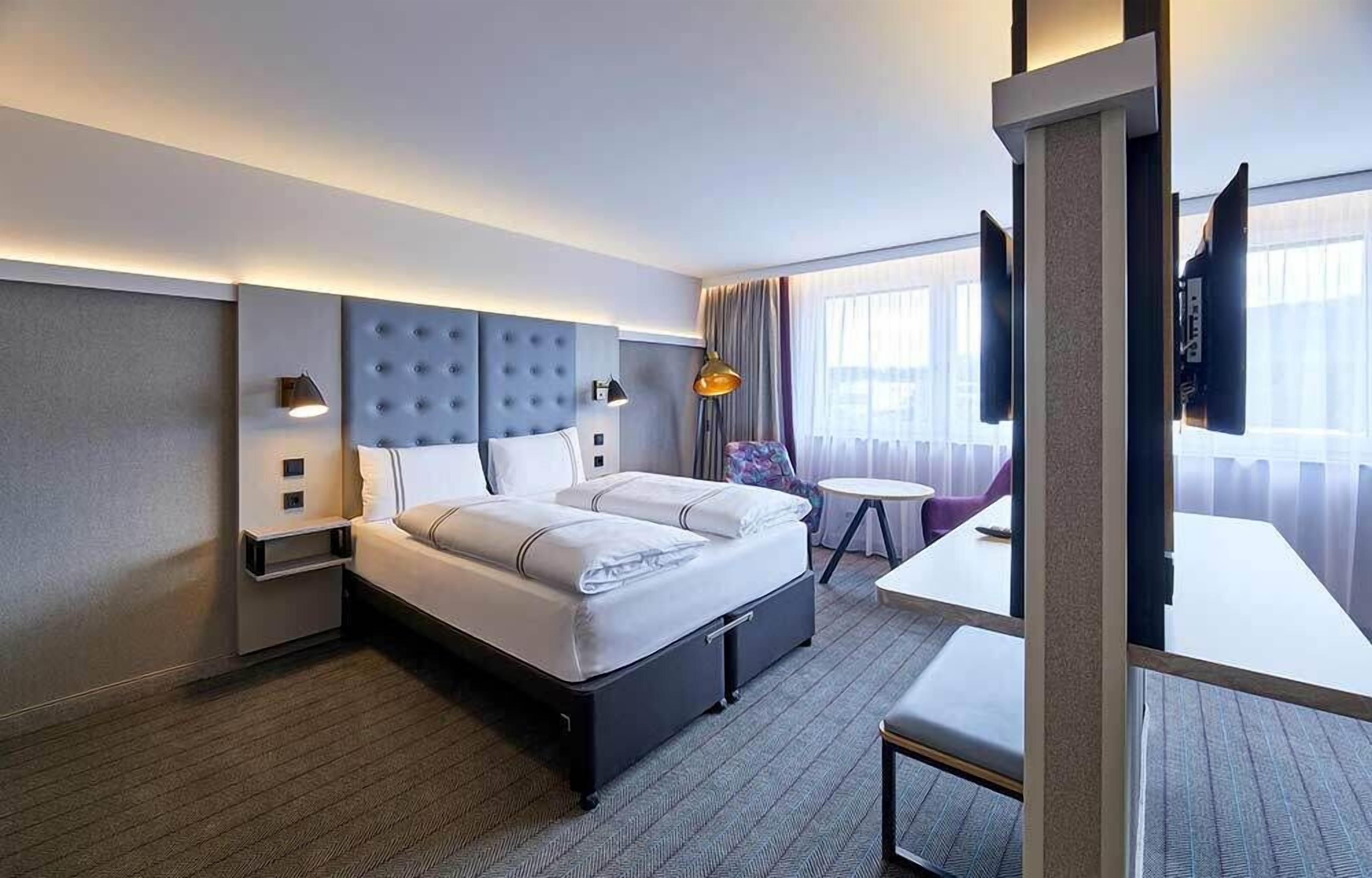 Ett modernt hotellrum med en stor säng, sängbord, ett litet bord och en TV.