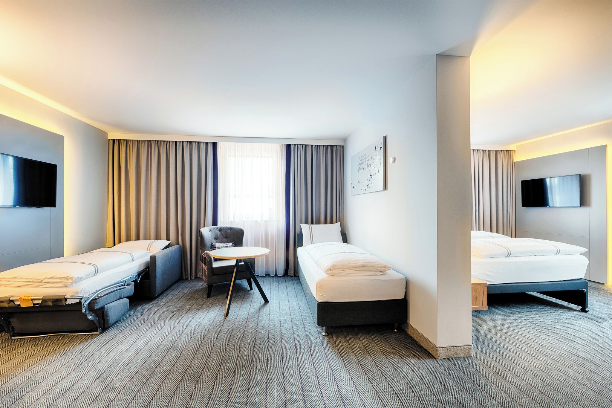 A hotel room with two single beds, a small table, a chair, a flat-screen TV, and a large window with curtains.