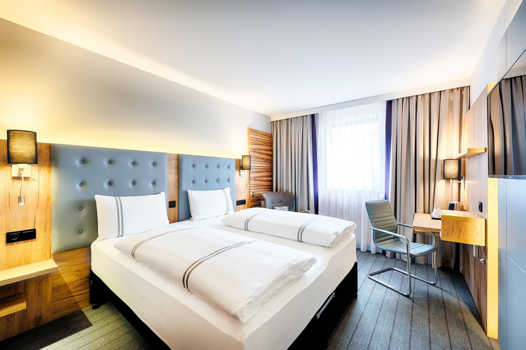Ett hotellrum med en stor säng, sängbord, ett skrivbord och en stol.