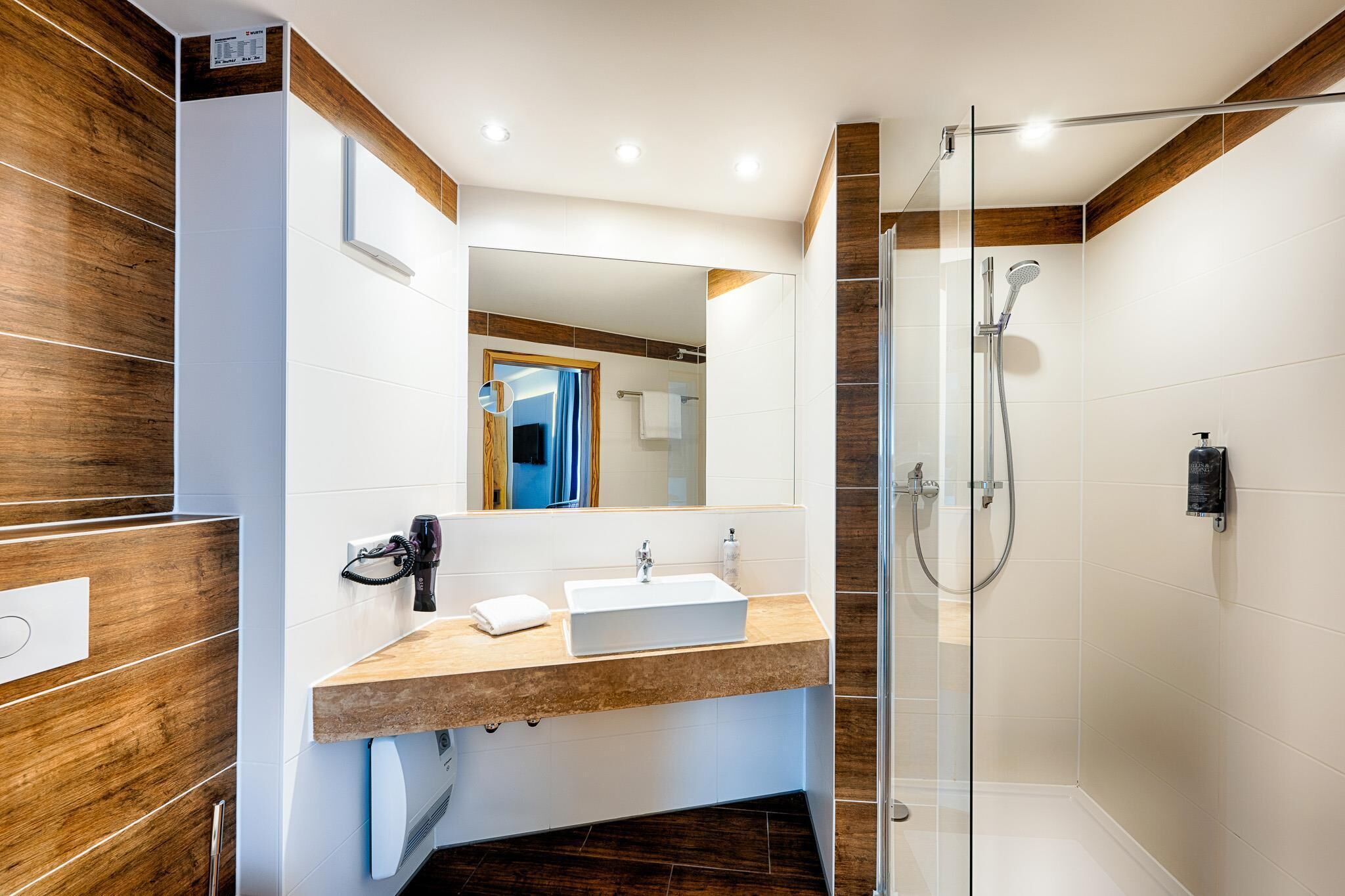 A modern bathroom with a glass shower enclosure, a white sink, and a wooden vanity.