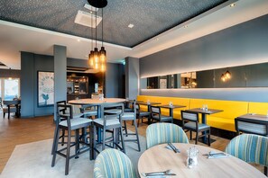 A modern restaurant with round tables, bar seating, and a yellow booth area. - Premier Inn Lindau (Lindau)
