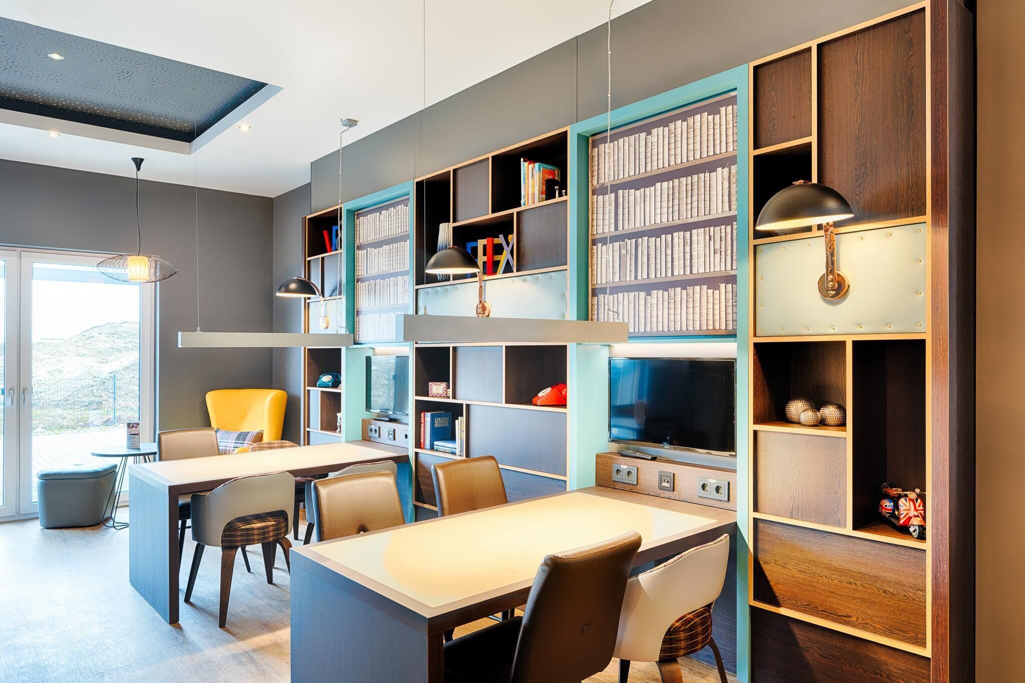 Una biblioteca moderna con estanterías, una zona de comedor y un televisor.