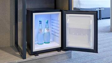 A compact refrigerator with two bottles of water inside, placed on a tiled floor near a bed.