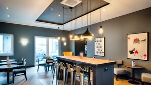 A modern bar area with a central island, bar stools, pendant lighting, and framed artwork on the walls. - Premier Inn Lindau (Lindau)