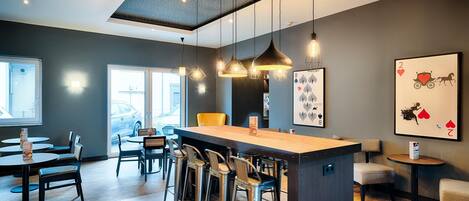 A modern bar area with a central island, bar stools, pendant lighting, and framed artwork on the walls.