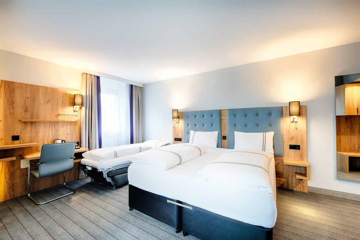 A hotel room with a large bed, a desk, a chair, and a wardrobe.