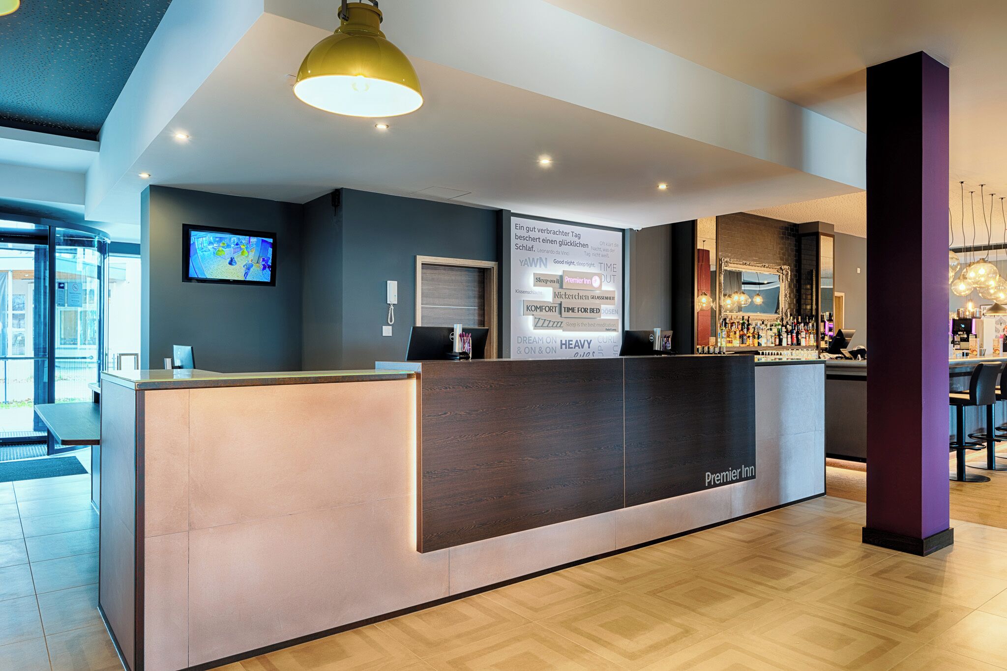 Zona de recepción de un hotel con diseño moderno, un mostrador de recepción, una pantalla digital y un área de bar.