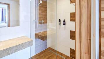 A modern bathroom with a glass shower enclosure, wooden flooring, and a built-in shelf.