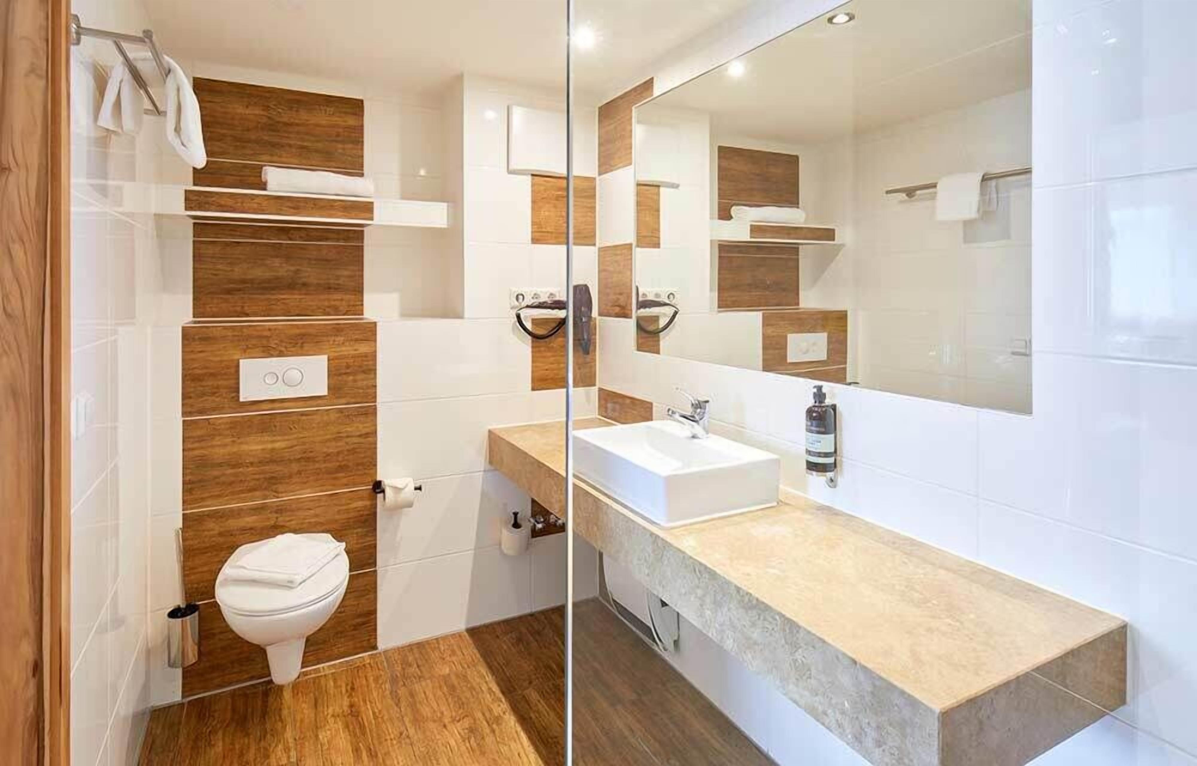 A modern bathroom with a wooden accent wall, a white sink, and a large mirror.