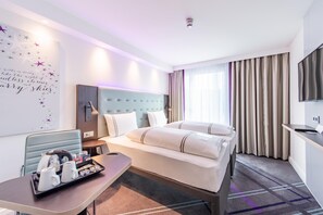 Hotellihuone, jossa on sänky, yöpöytä ja seinälle asennettu televisio.