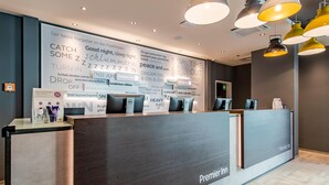 Een hotel receptiebalie met donker houten afwerking, een digitaal scherm en een bord waarop staat dat het een Premier Inn is.