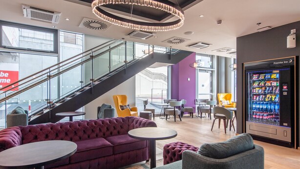 Een moderne hotel lobby met een trap, zithoek en een automaat.