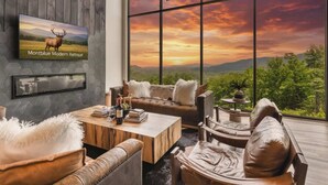 A modern retreat room with a large window, a ceiling fan, and a mounted television displaying a mountain scene. - Incredible Mountain Views | Indoor Pool | Luxury (Sevierville)