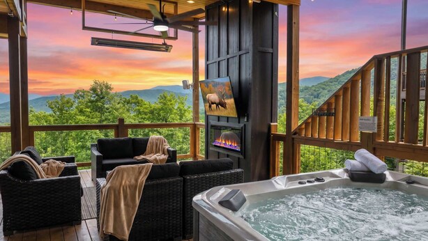 A wooden deck with a hot tub, wicker furniture, a fireplace, and a scenic mountain view. - Incredible Mountain Views | Indoor Pool | Luxury (Sevierville)