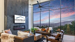 A modern living room with a large window offering a scenic view, a fireplace, and a sign for MontBlue Modern Retreat. - Incredible Mountain Views | Indoor Pool | Luxury (Sevierville)