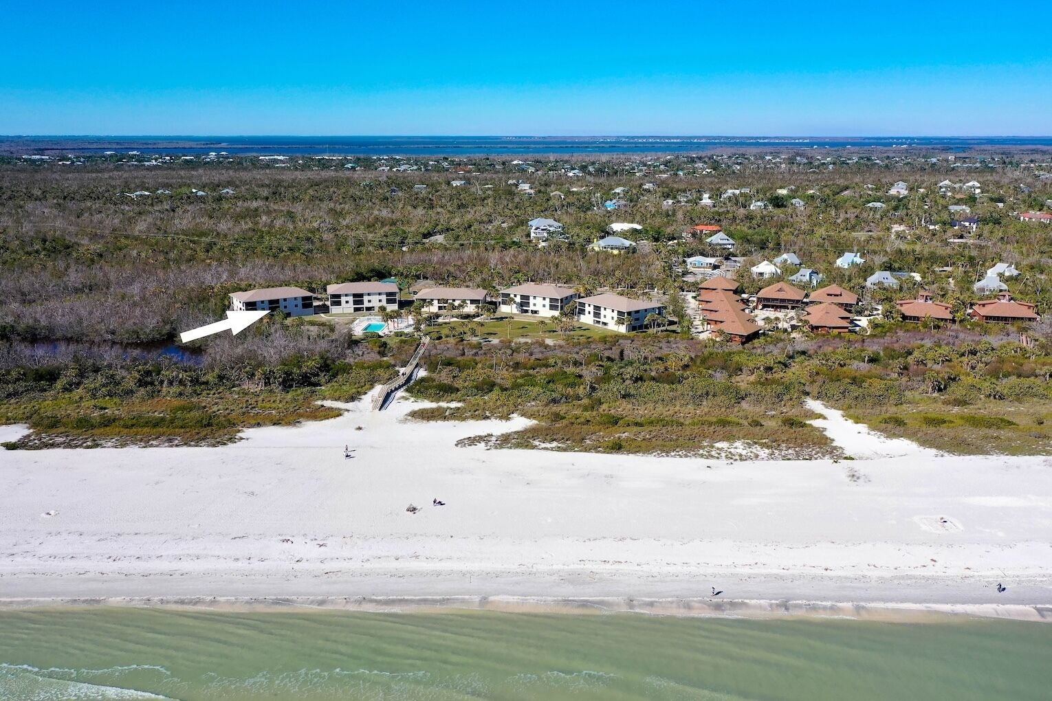 An aerial view of a coastal area with multiple buildings, a beach, and a clear sky.