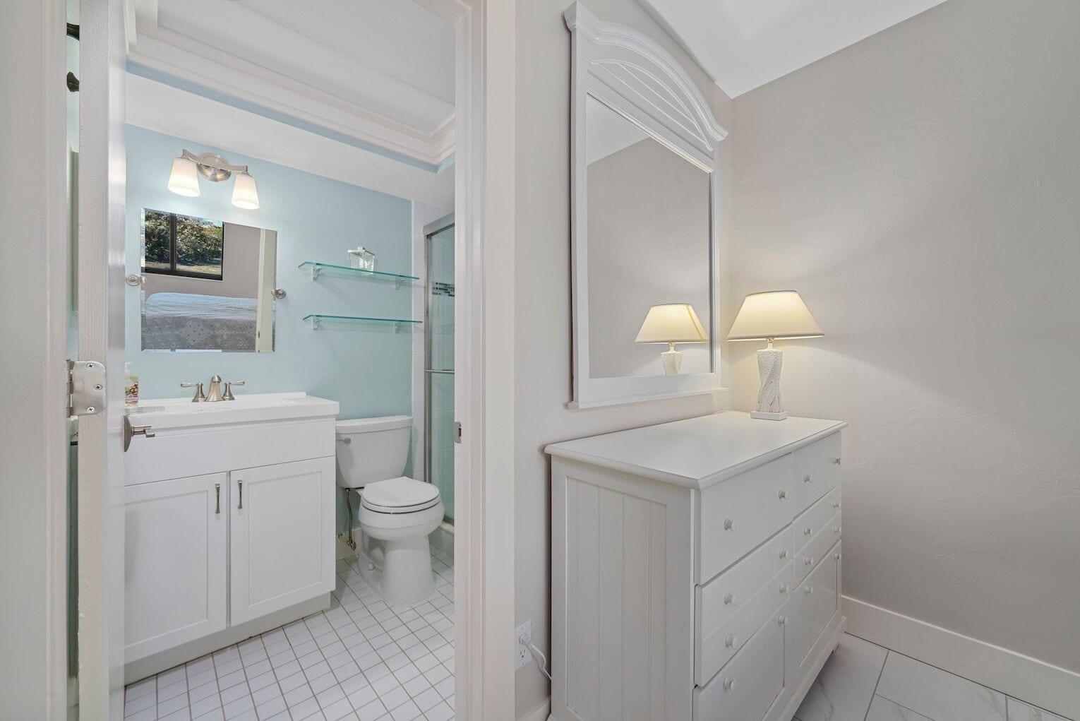 A bathroom with a white vanity, a glass shower enclosure, and a large mirror with two lamps.