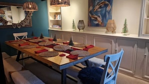 Un coin repas avec une table en bois dressée pour quatre personnes, entourée de chaises, et un petit sapin de Noël accroché au mur.