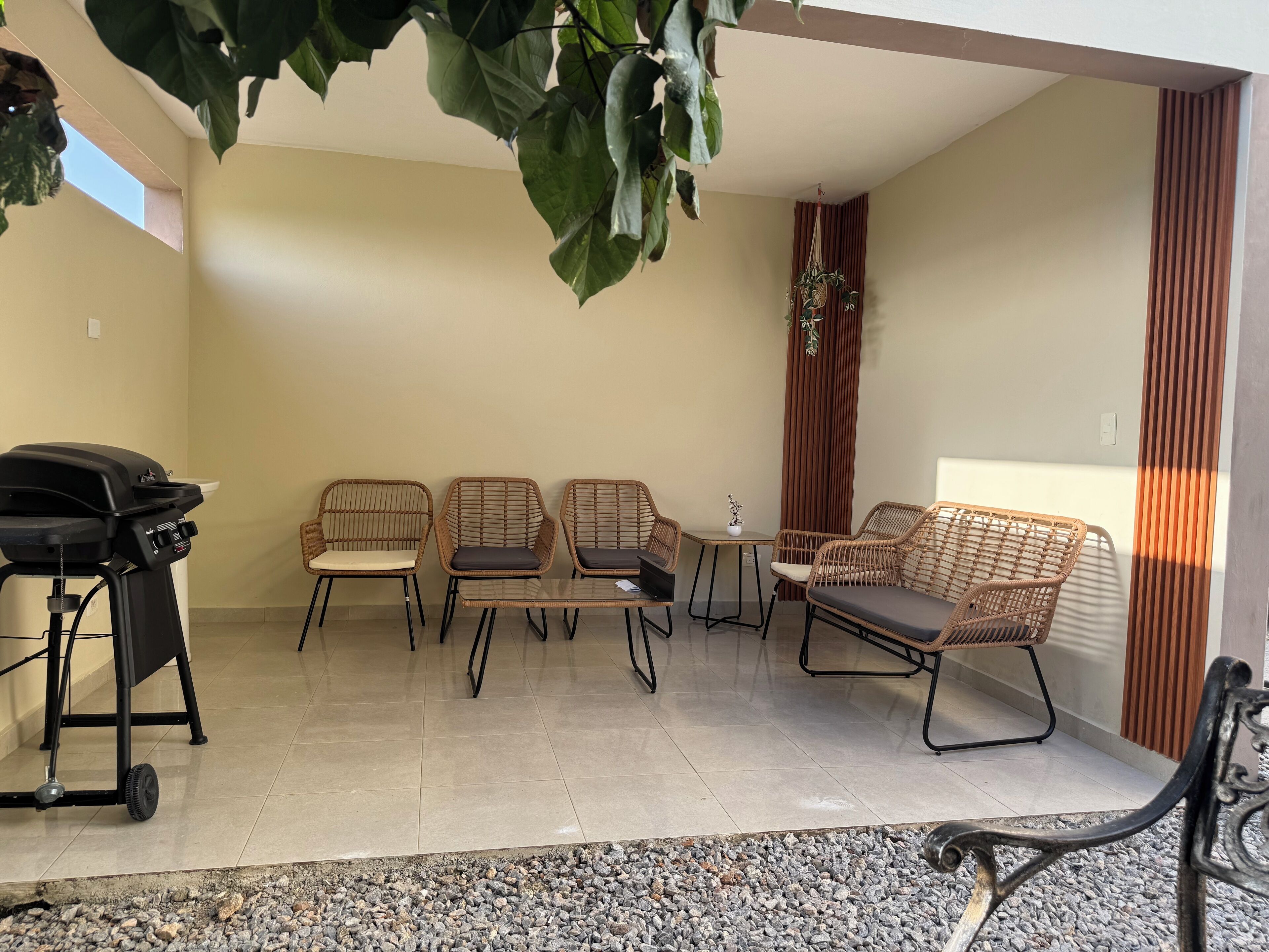 Un'area patio con mobili in vimini, un barbecue e un tavolino con una pianta.