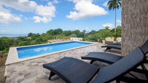 A swimming pool with lounge chairs, surrounded by stone tiles and palm trees, overlooking a lush landscape. - Casa Vista Mar 1 (Rio San Juan)