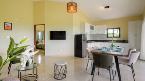 A modern kitchen with white cabinets, a dining table set for four, and a television mounted on the wall. - Casa Vista Mar 1 (Rio San Juan)