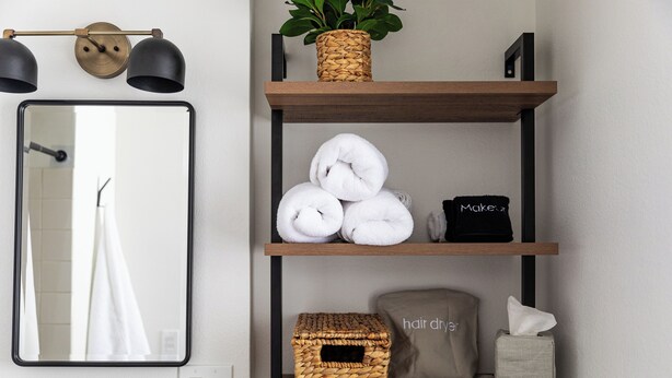 A bathroom with a mirror, shelves with towels, a hair dryer, and a basket. - The Windmoor Lodge (Grayling)