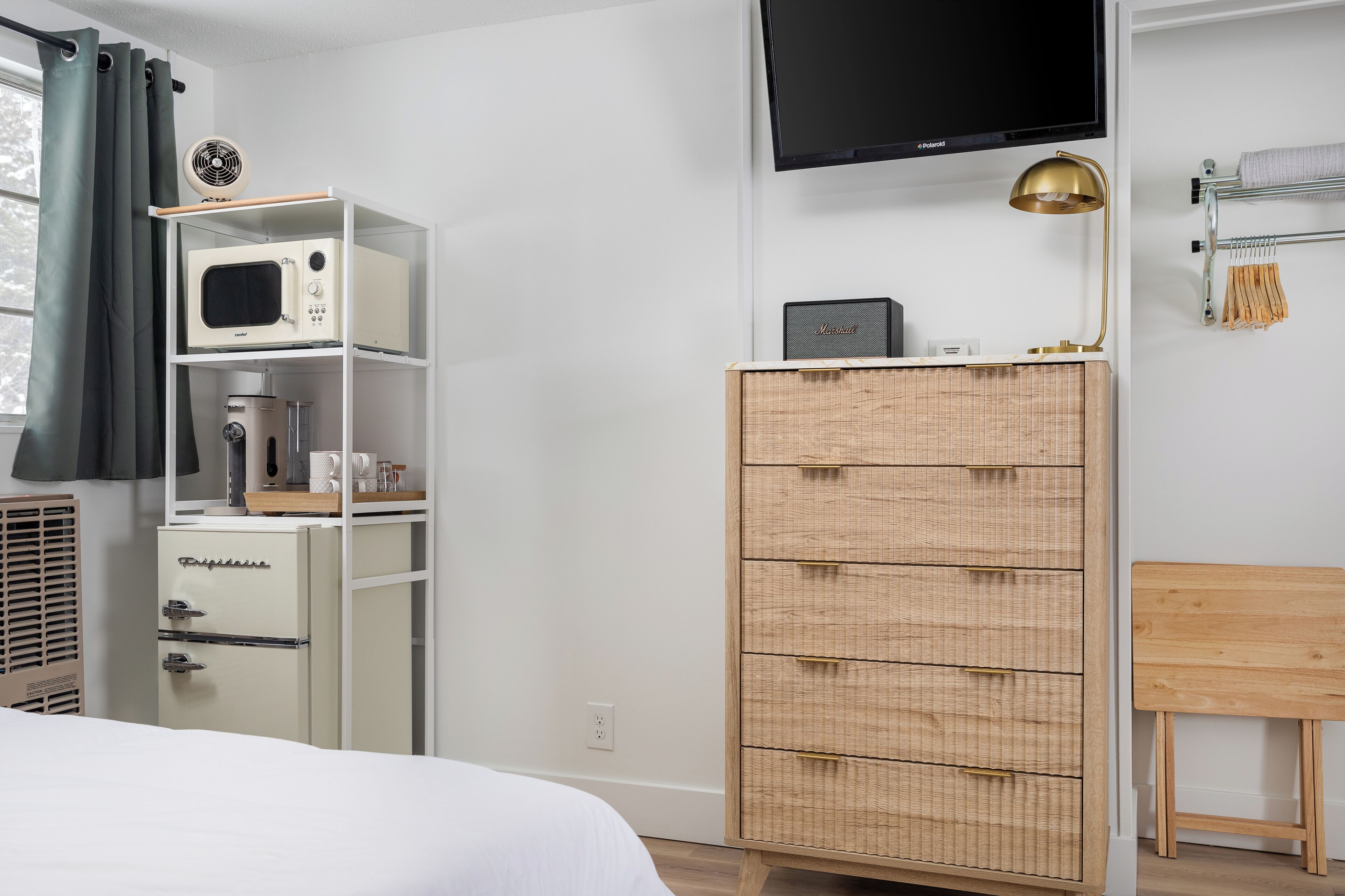 A bedroom with a bed, a white wardrobe, a wicker dresser, a flat-screen TV, and a bedside table.
