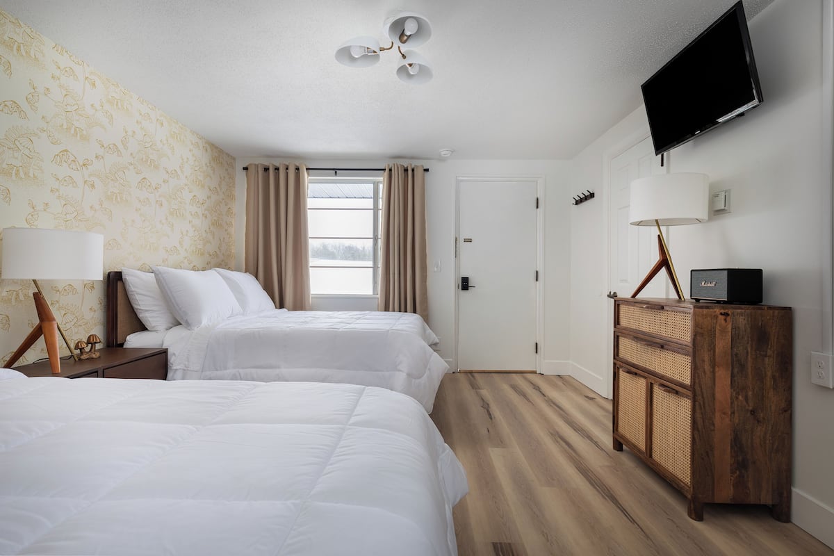 A hotel room with two beds, a TV, a lamp, and a wooden dresser.