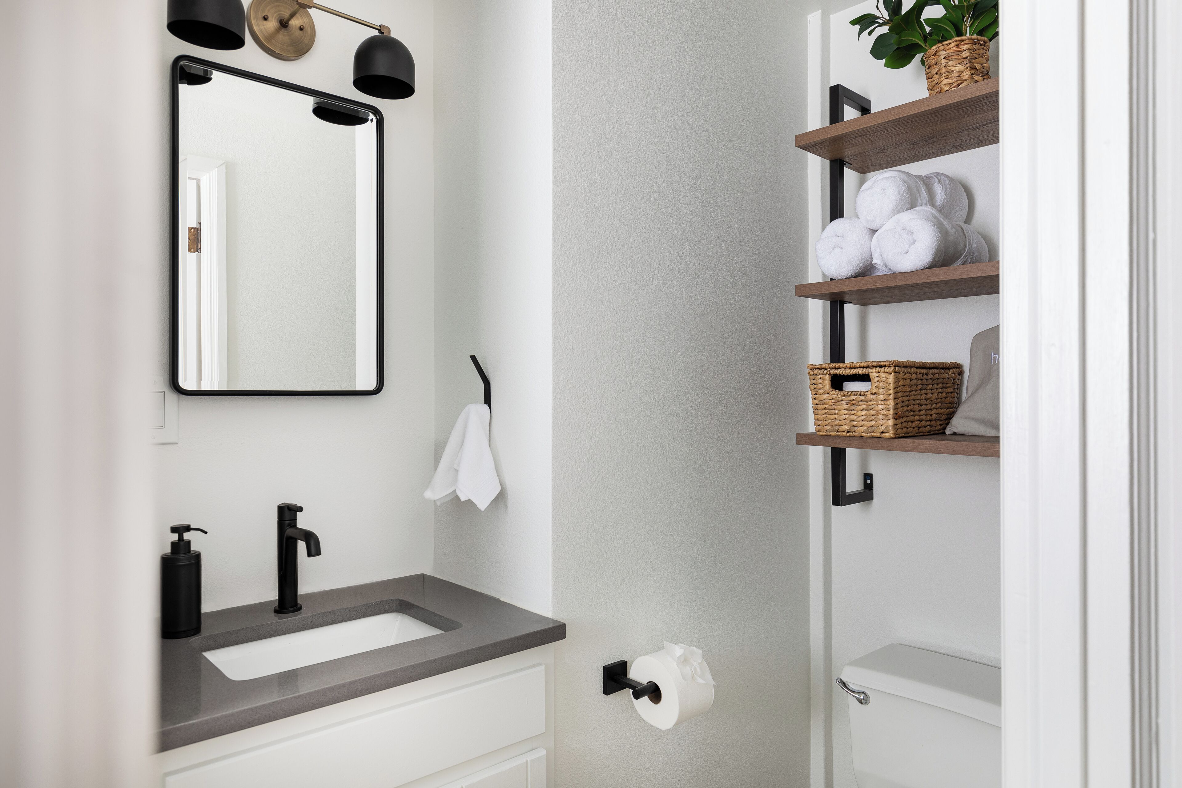 Un baño moderno con un espejo grande, grifo negro y un perchero.