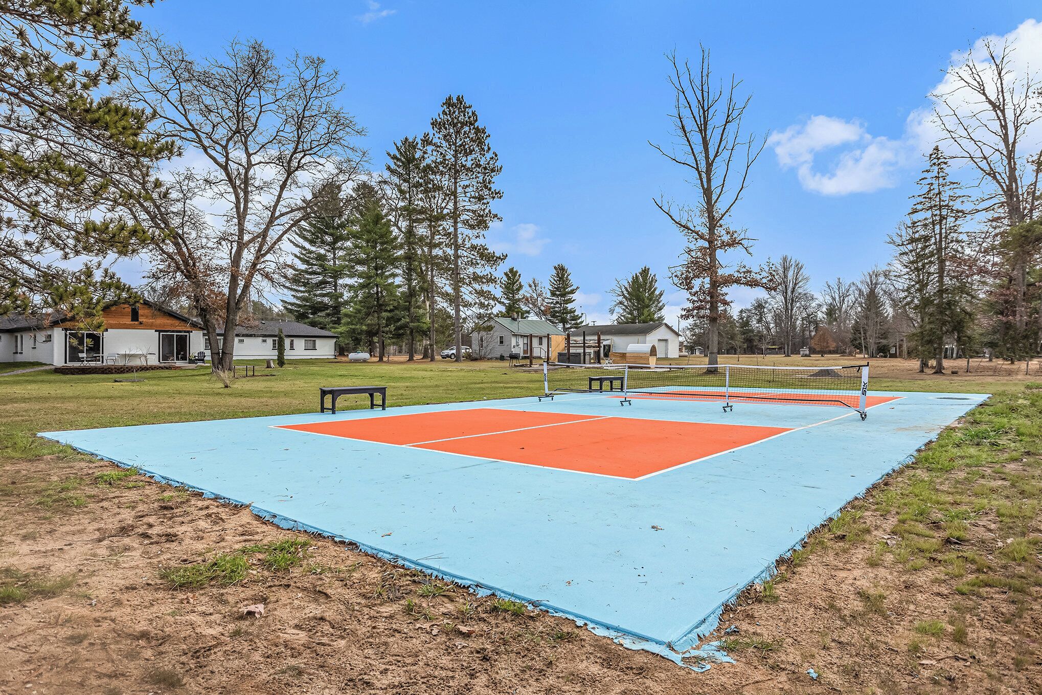 A tennis court with a net, surrounded by trees and houses.