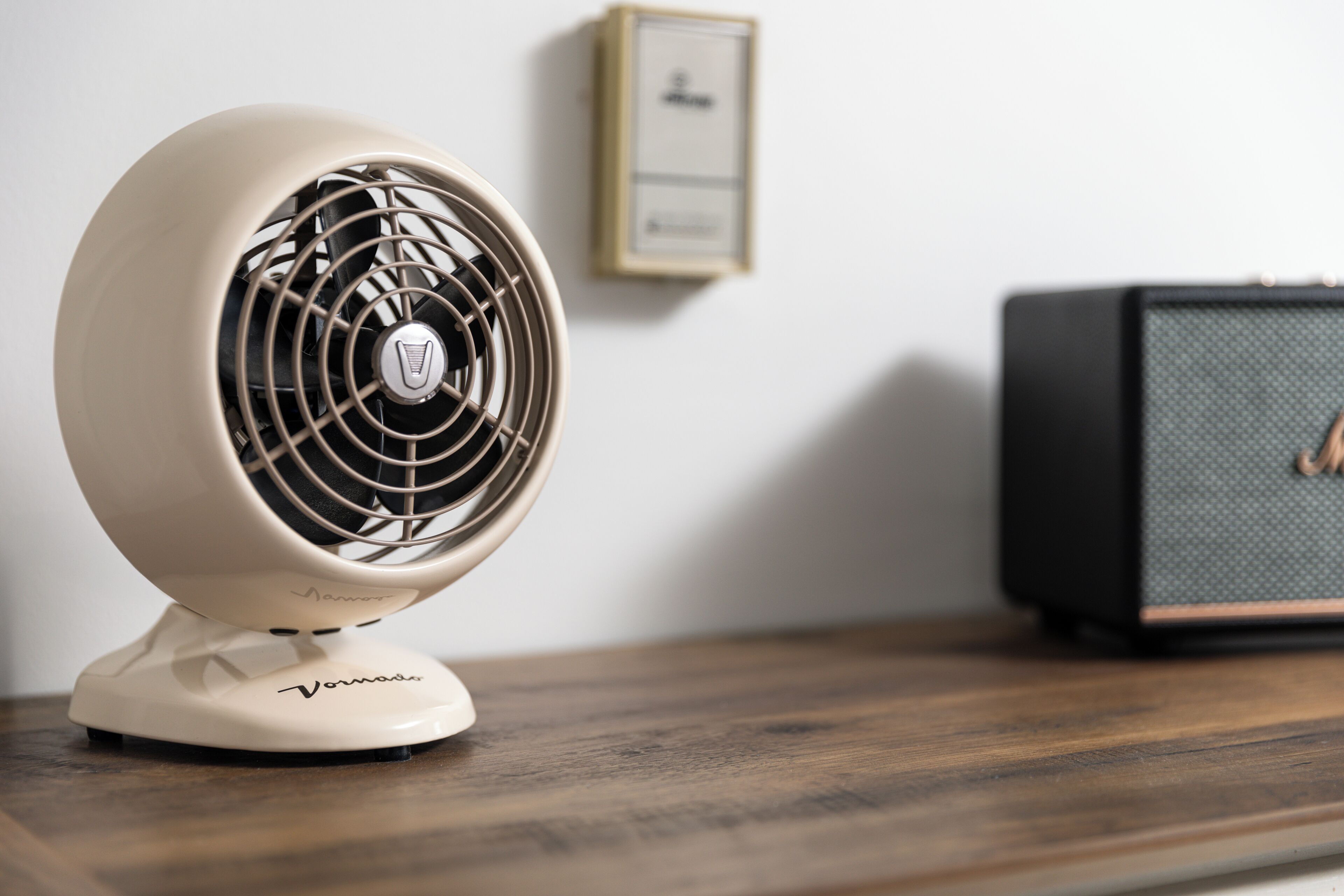 A vintage-style fan on a wooden table with a speaker in the background.