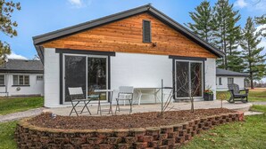 A modern house with a white exterior and wooden roof, featuring a patio with outdoor furniture and a brick garden bed. - The Windmoor Lodge (Grayling)