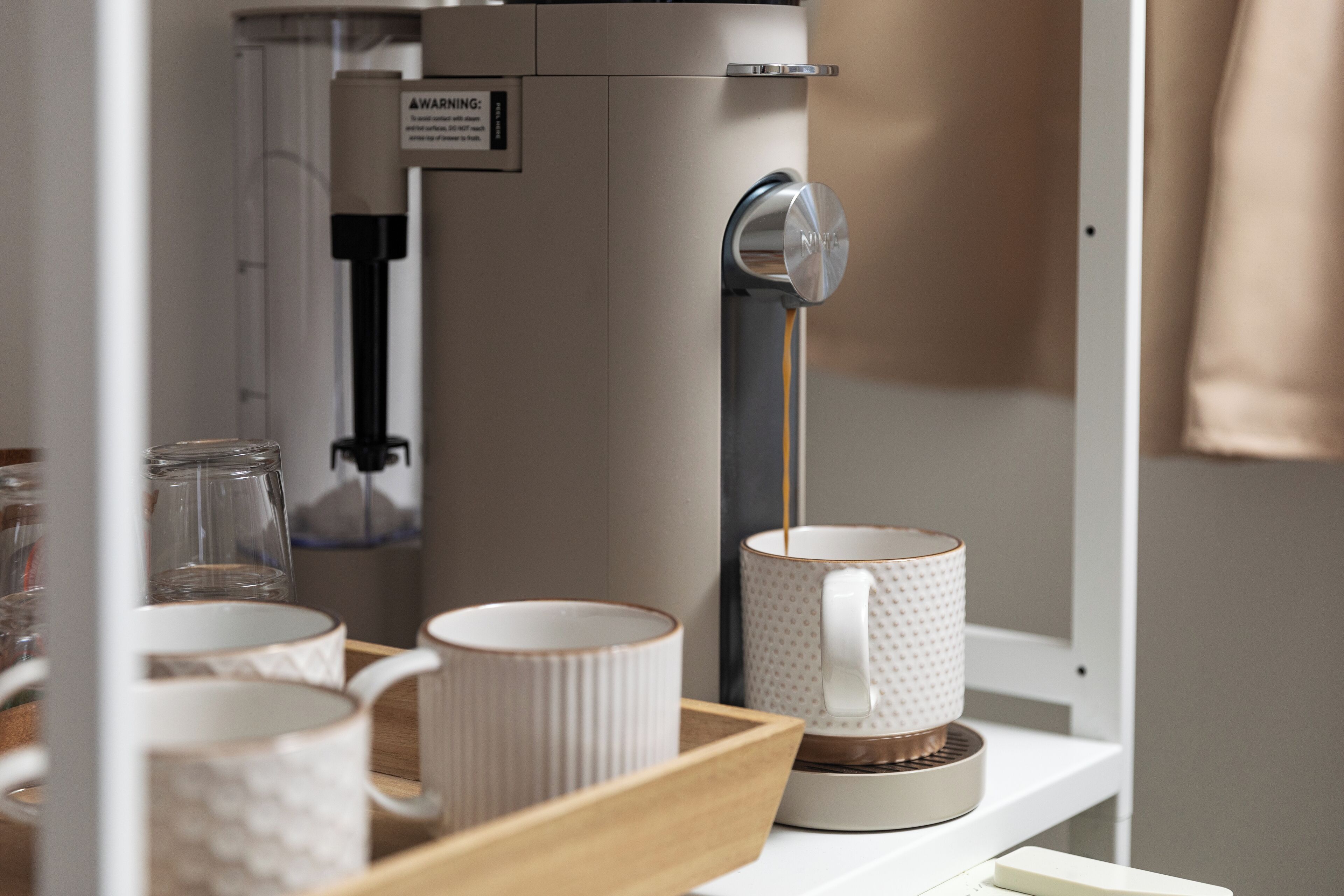 A coffee machine dispensing coffee into a mug, with a tray of cups and a glass container nearby.