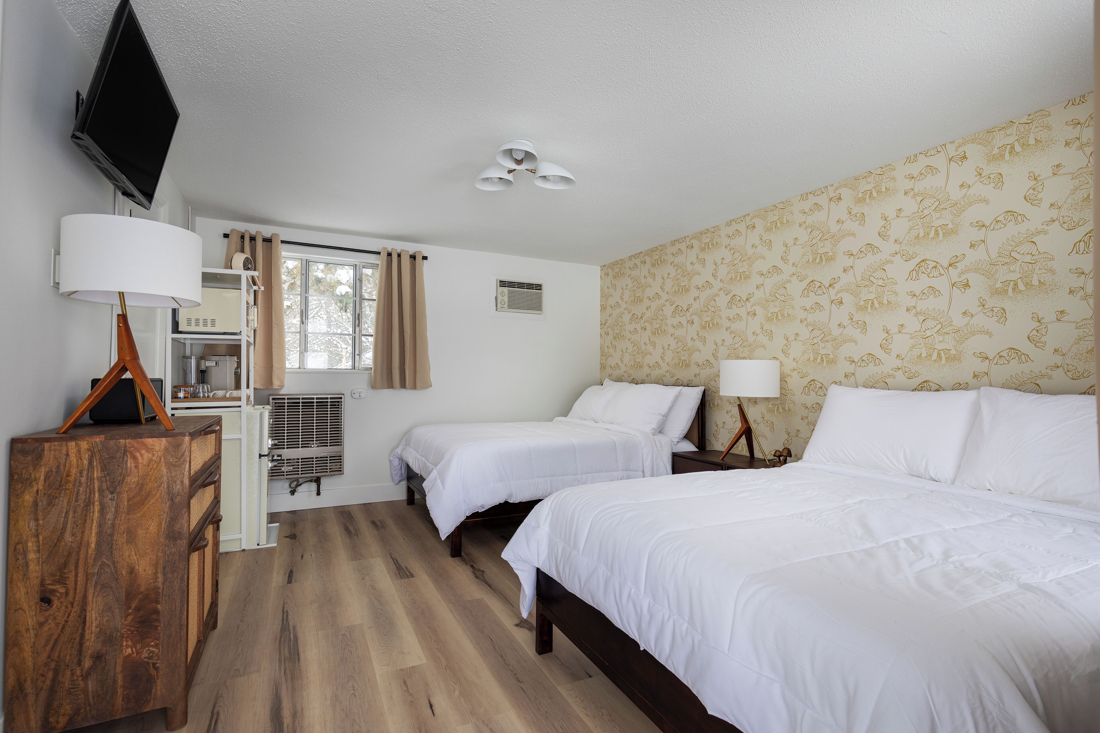 A hotel room with two beds, a wooden dresser, a flat-screen TV, a ceiling fan, and a window with curtains.