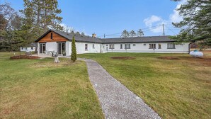 A two-story house with a gravel driveway leading to a wooden deck. - The Windmoor Lodge (Grayling)