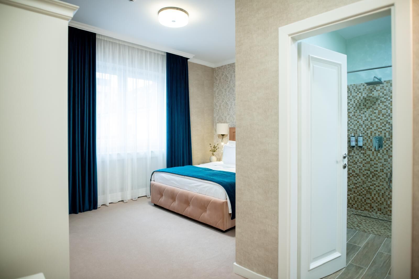 Una habitación de hotel con cama, baño con ducha y puerta que da a otra habitación.